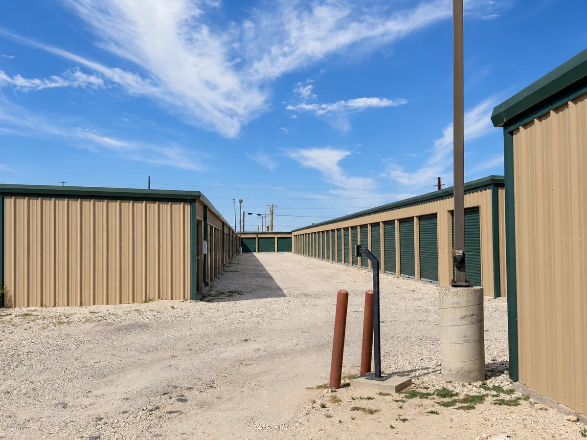 Gravel driveway between tan storage buildings with green roll-up doors